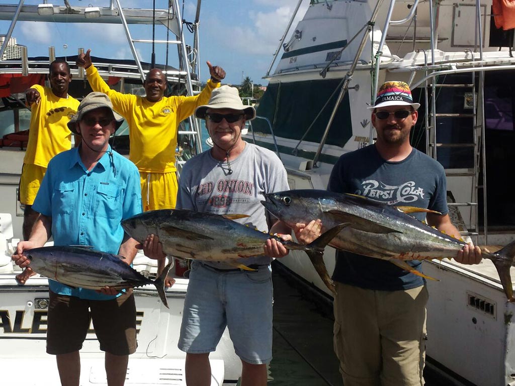 Three anglers taking a photo with the Tuna they caught during a fishing trip in Jamaica with the boat crew in the background.