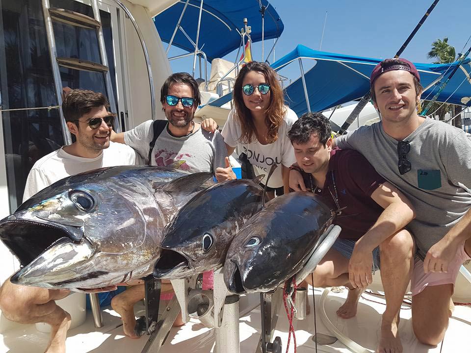 A group of anglers back on the dock after a successful fishing trip in Tenerife hold three Tunas they caught