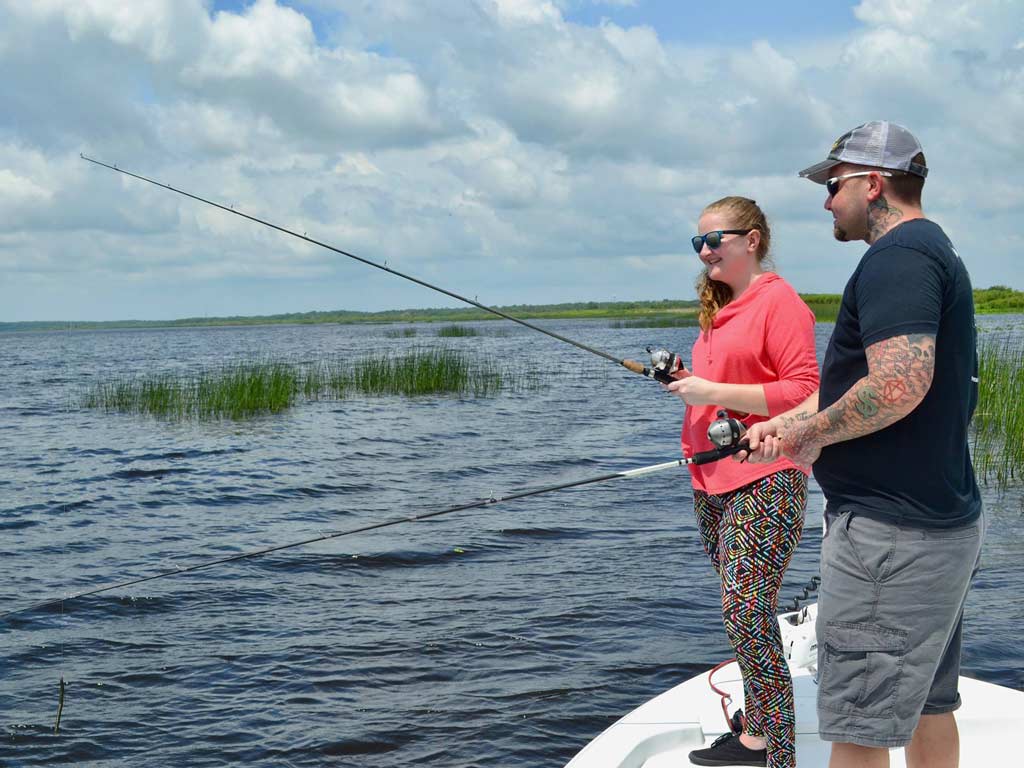 Two anglers standing on a boat, holding rods and fishing for Bass. 