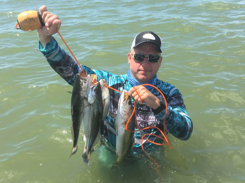 A photo of an angler standing in the water up to his waist and showing off the fish he caught wade fishing in Trinity Bay