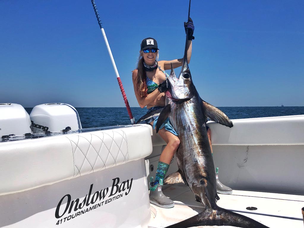 A female angler holds a large Swordfish boated on a deep sea fishing trip.