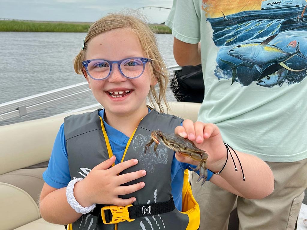 A young girl in a safety vest holds up a crab she just caught somewhere near Corolla, NC.