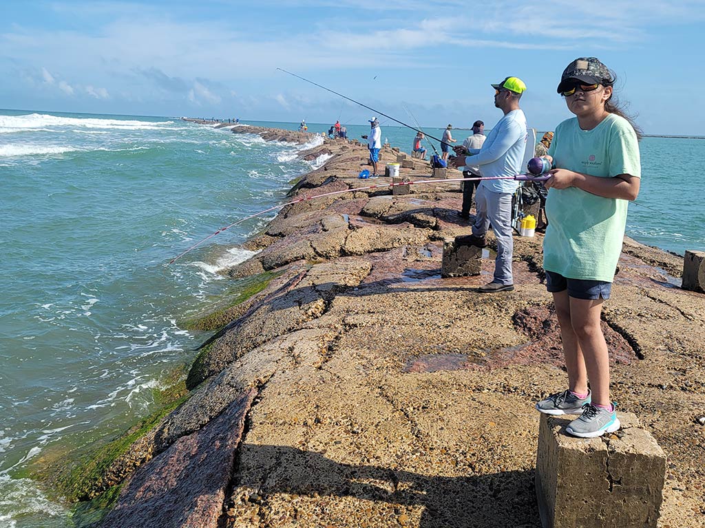 A group of anglers fishing on a jetty in South Padre Island on a sunny day