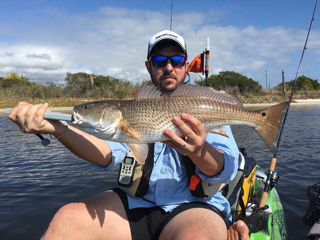 An angler holds a Redfish while sat on a kayak inshore in Destin, FL