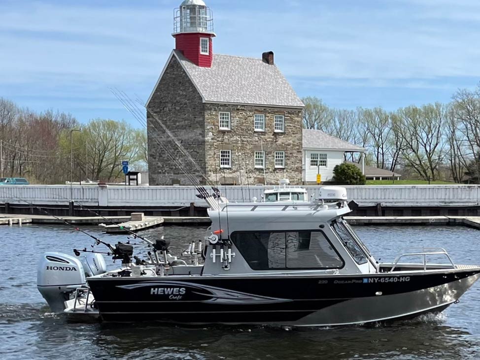 A fishing charter gently moving along the Salmon River in front of a lighthouse