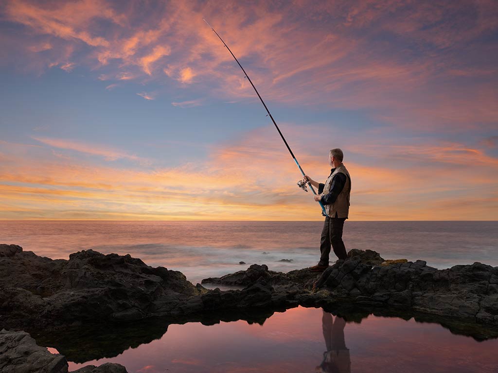 A rear-view image of an angler casting into the surf in Tenerife at sunset