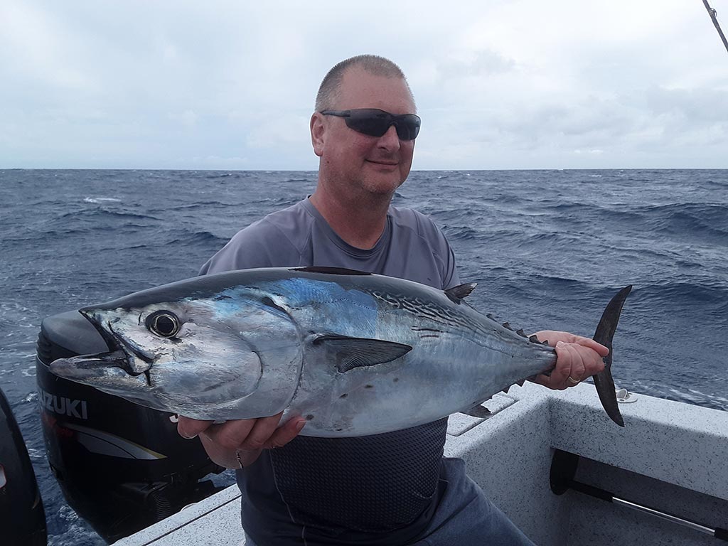A fisherman wearing sunglasses holds up a tuna he caught in the Gulf Stream during a fishing trip.