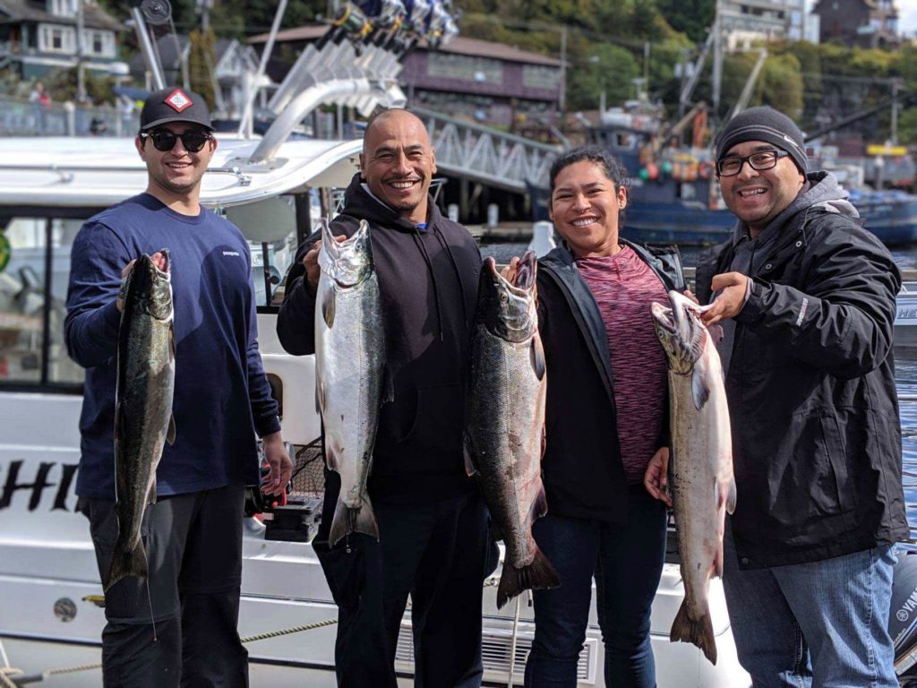 A picture showing a group of anglers, each holding a freshly-caught Salmon while standing on a dock in Ketchikan, Alaska