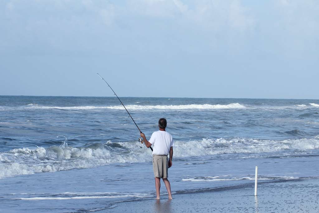 A man standing in the surf, holding a fishing rod, with his line in the water