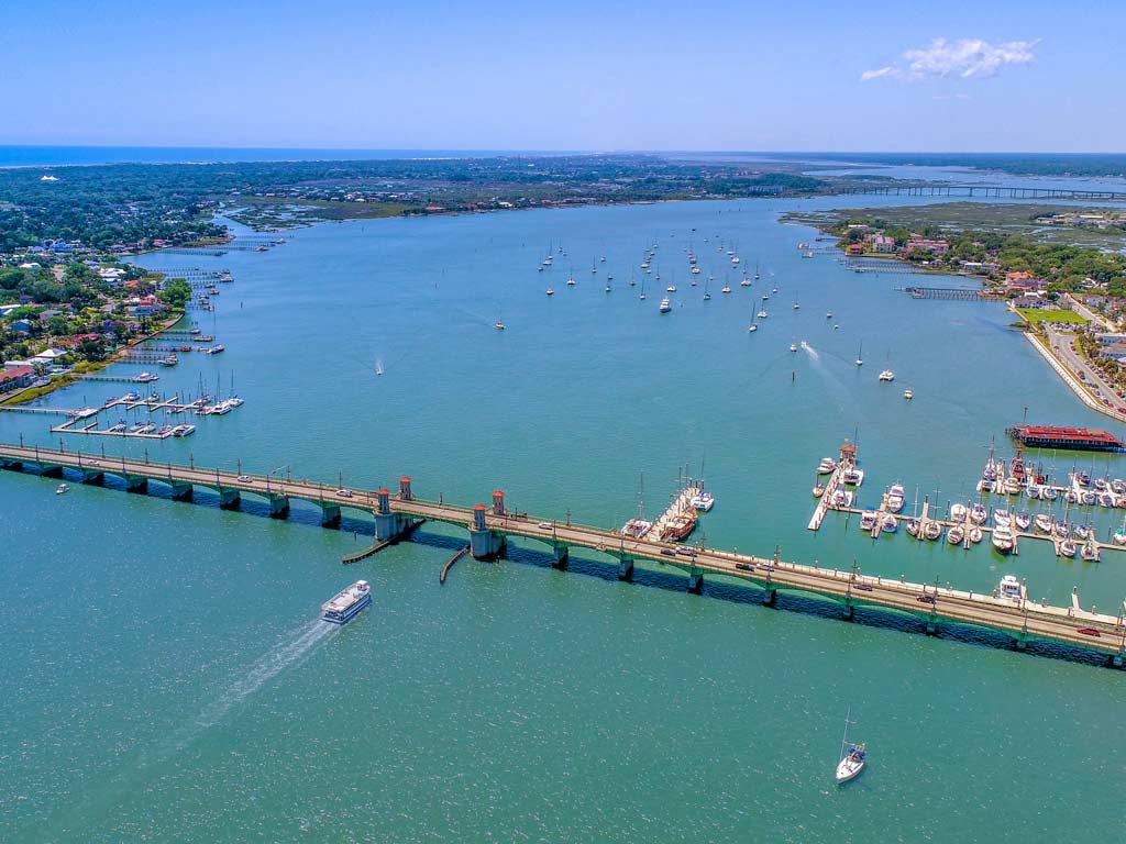 An aerial photo of the Bridge of Lions in St. Augustine, Florida on a clear day, with boats in the water behind it.