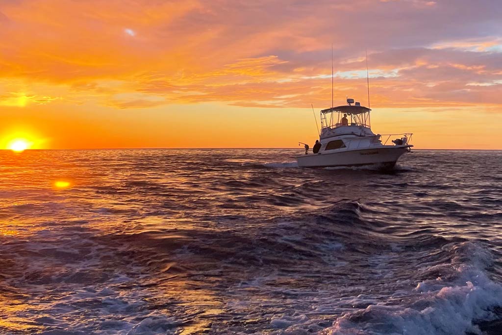 A charter boat on choppy waters at sunset, with anglers on the deck fishing