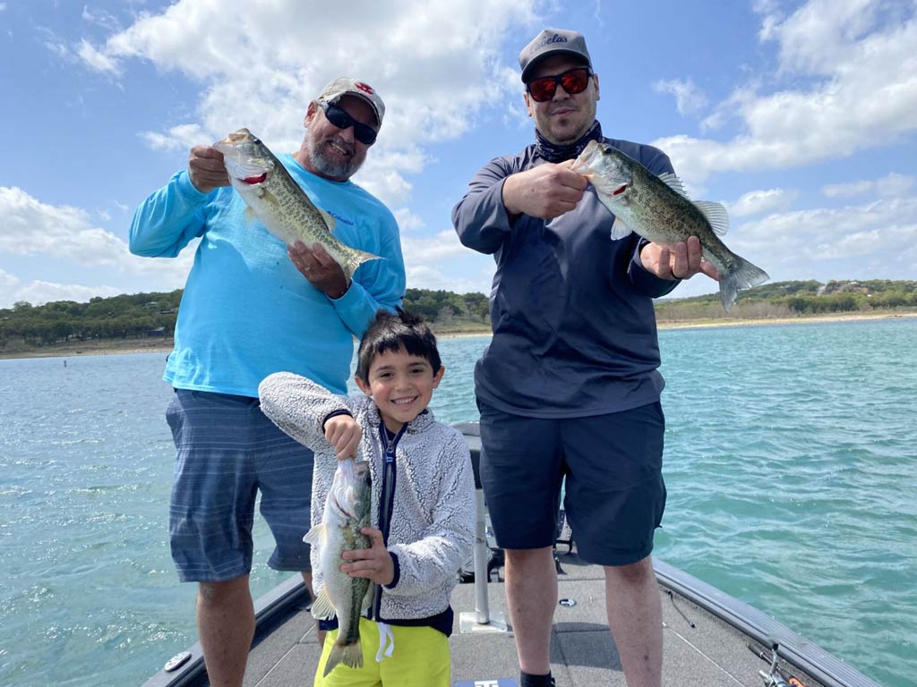 A photo of two adult anglers and a child standing on a charter fishing boat and happily showing off their catches on a bright and sunny day