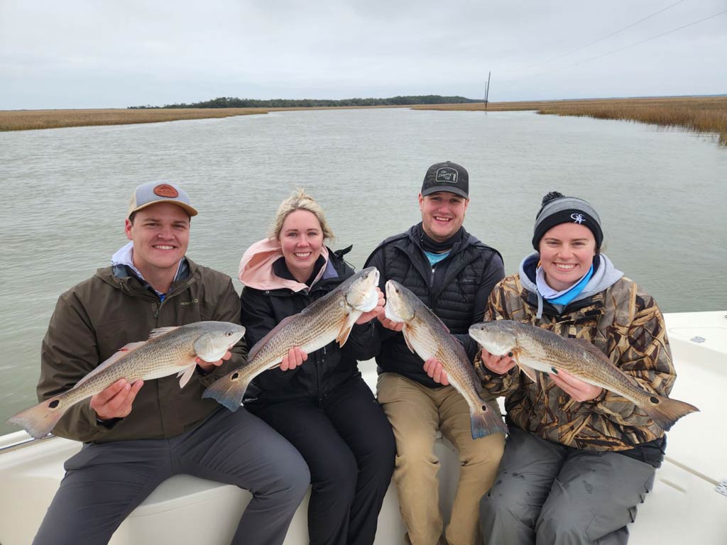 Four anglers sitting on a fishing charter boat on a cloudy winter day in South Carolina and holding the fish they caught there