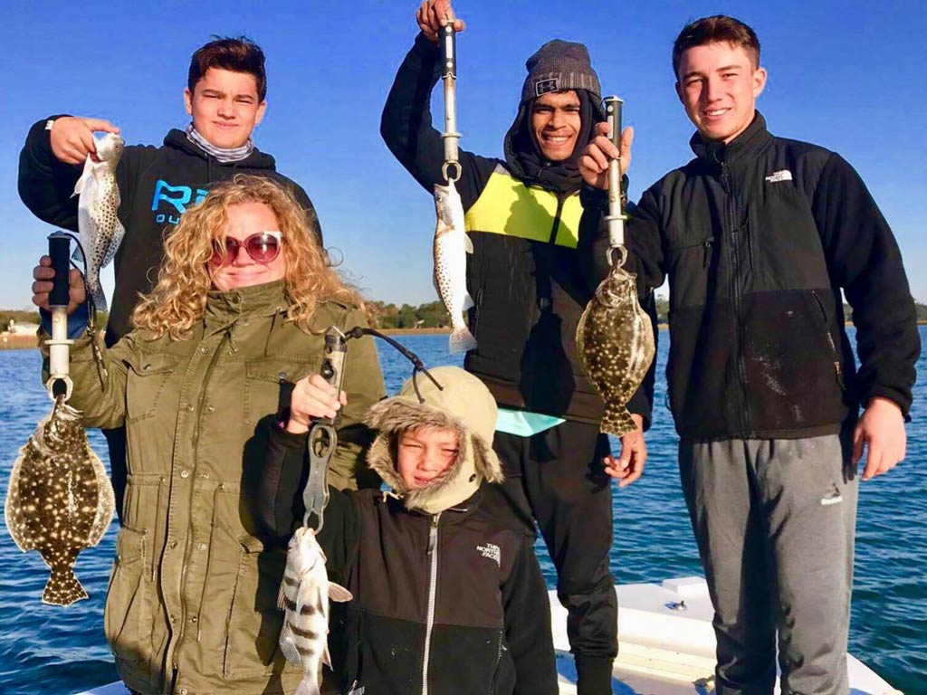 A group photo of three anglers and a kid standing on a boat and posing with their catches during South Carolina’s fall fishing season