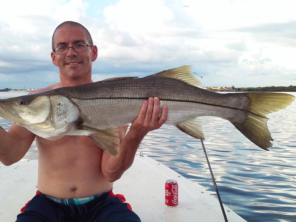 A male angler wearing eyeglasses, sitting on a charter fishing boat operated by Florida Professional Charters and holding a large Snook, Tampa, Florida