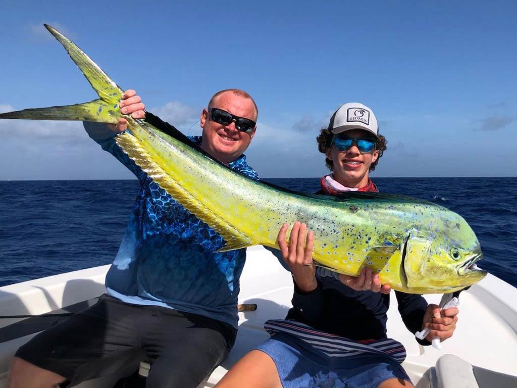 A photo of two anglers sitting on a charter boat and holding big Mahi Mahi during a summer season in South Carolina