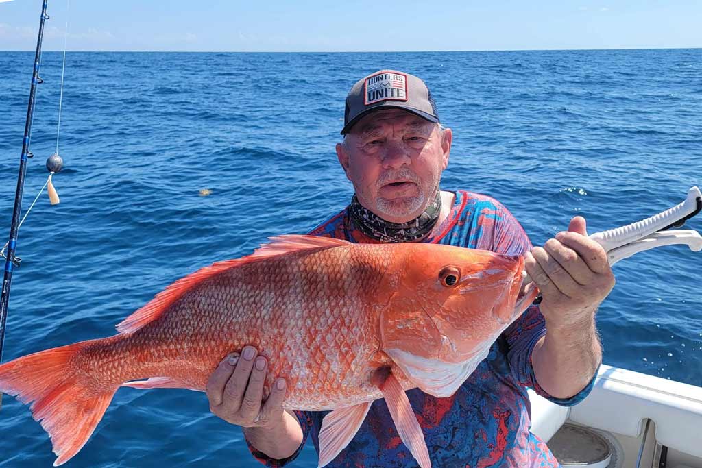 An elderly fisherman holding a big Red Snapper, with water in the background