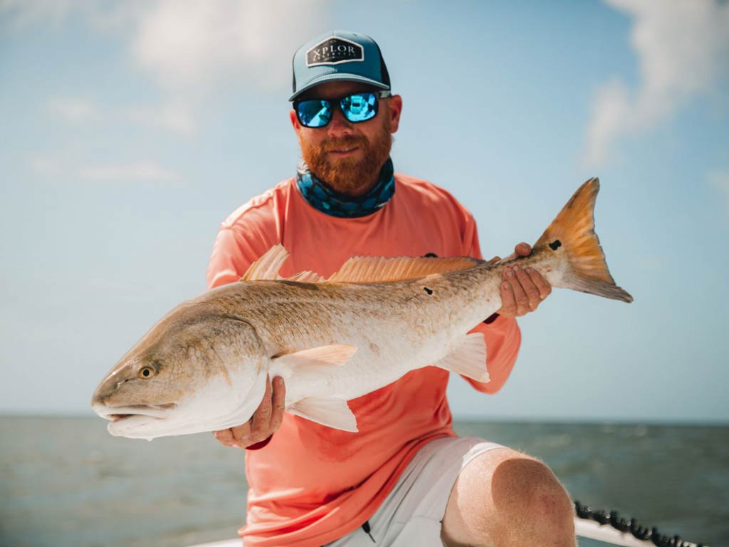 A high-quality photo of an angler holding a big Redfish on a bright late summer's day