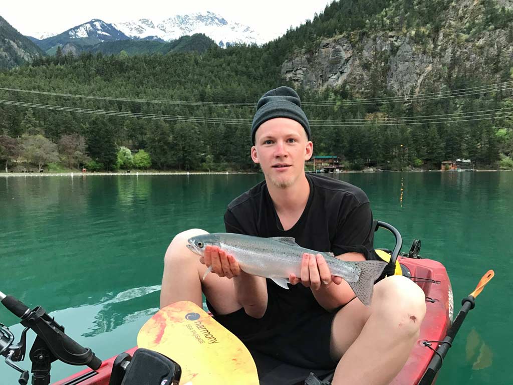 A kayak angler holding a Rainbow Trout caught fishing on Seton Lake, and presenting it to the camera.