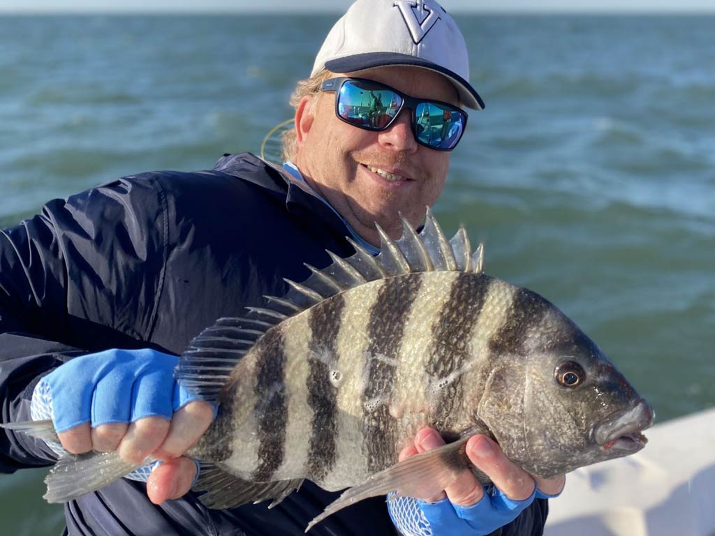 An angler in sunglasses holding a Sheepshead with both hands in front of him