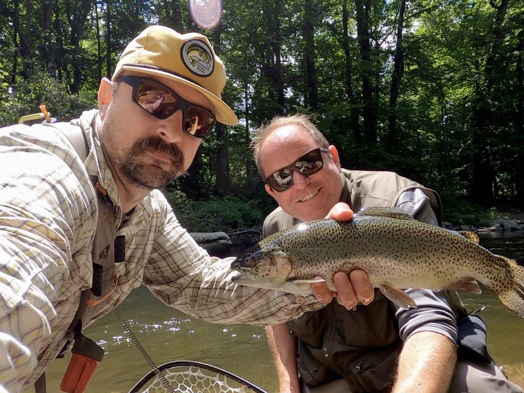 A photo of two fly fishing anglers squatting and taking a selfie with a Trout caught in Asheville during springtime