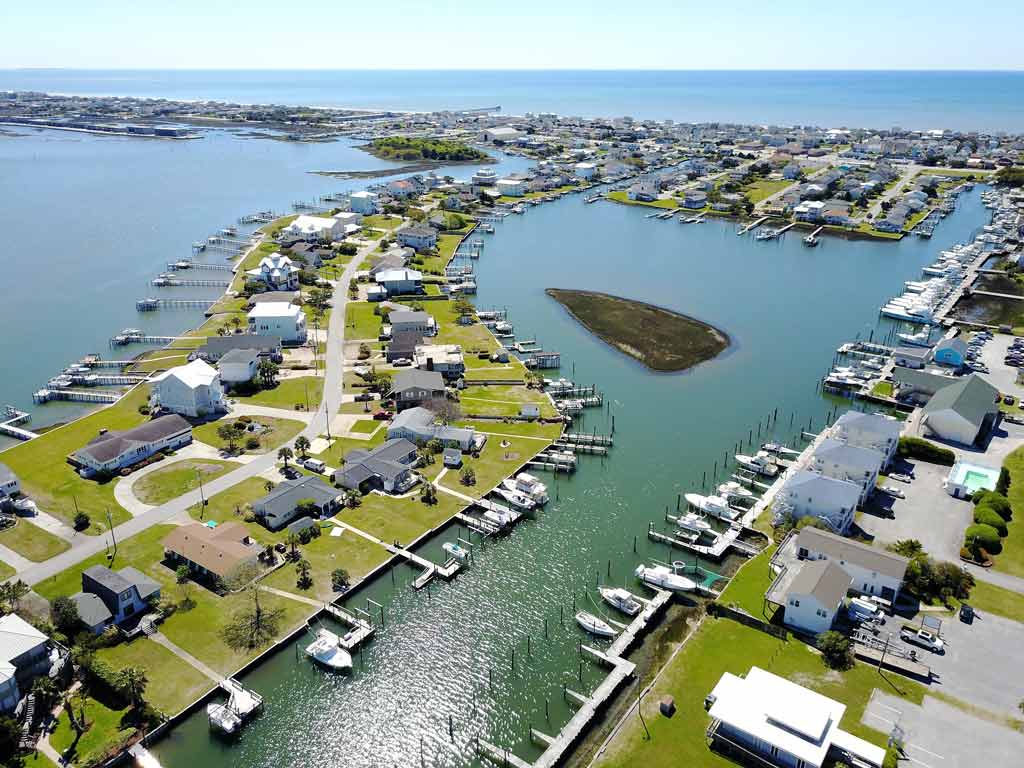 An aerial photo of Atlantic Beach, which is part of North Carolina's Crystal Coast, with waterfront houses, each featuring a fishing dock, visible in the foreground and the Atlantic Ocean seen in the distance. 