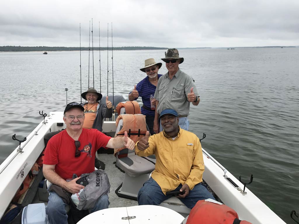 A photo of five anglers smiling at the camera and posing with their thumbs up while on a charter boat getting ready to fish on Lake Texoma on a cloudy spring day