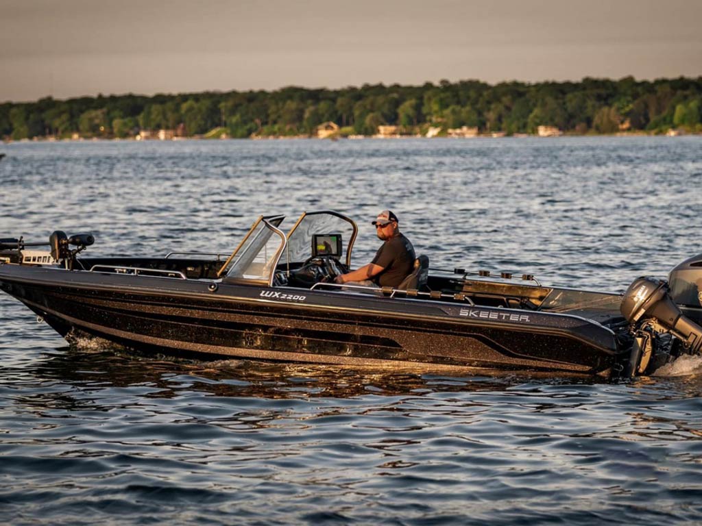 A side view of a guide sitting in his charter fishing boat and navigating the Fox River in the proximity of the shore at sunset