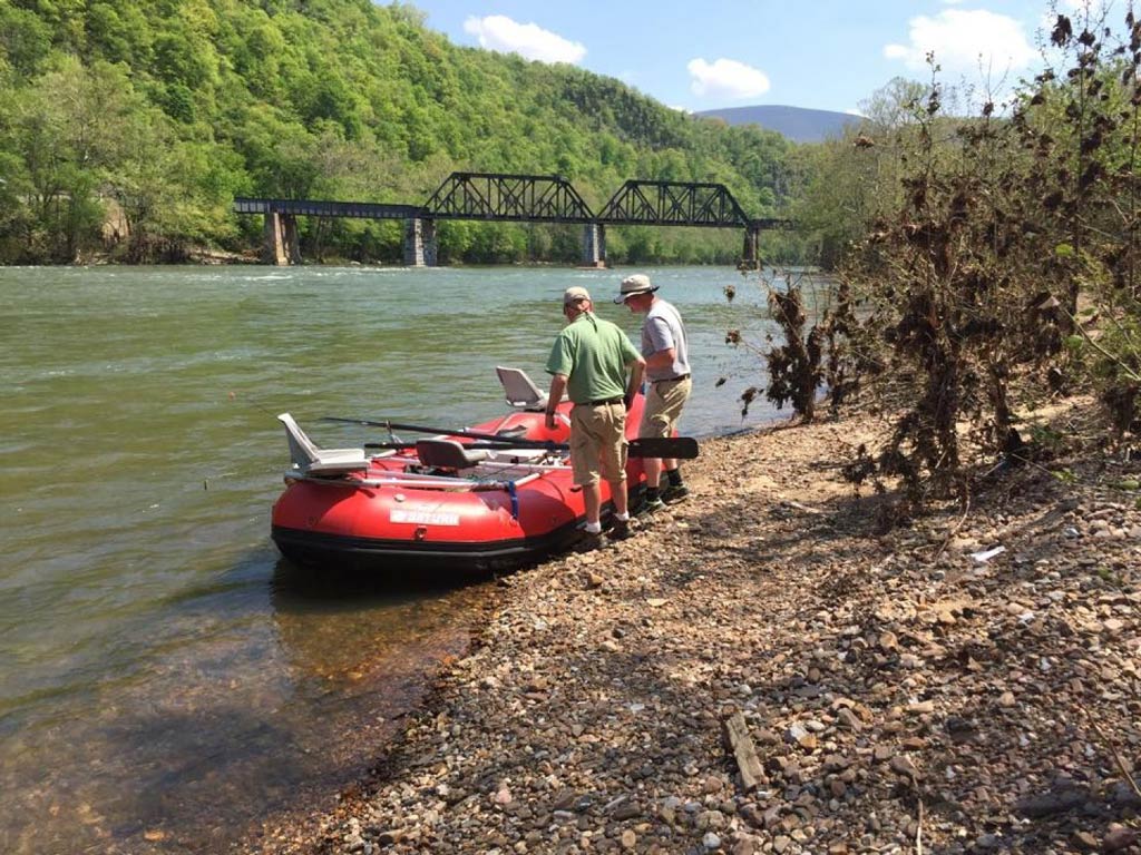 A photo of two anglers standing on the shore next to a kayak getting ready to go kayak fishing on the Tennessee River on a bright and sunny spring day