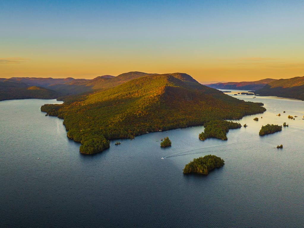 A scenic aerial photo of the middle portion of Lake George, called the Narrows, with a forest hill and numerous small islands visible, surrounded by water.