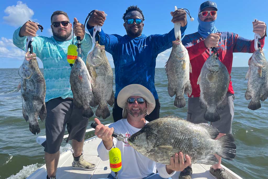 A group of smiling fishermen standing on a charter fishing boat, each holding one or two Tripletail fish