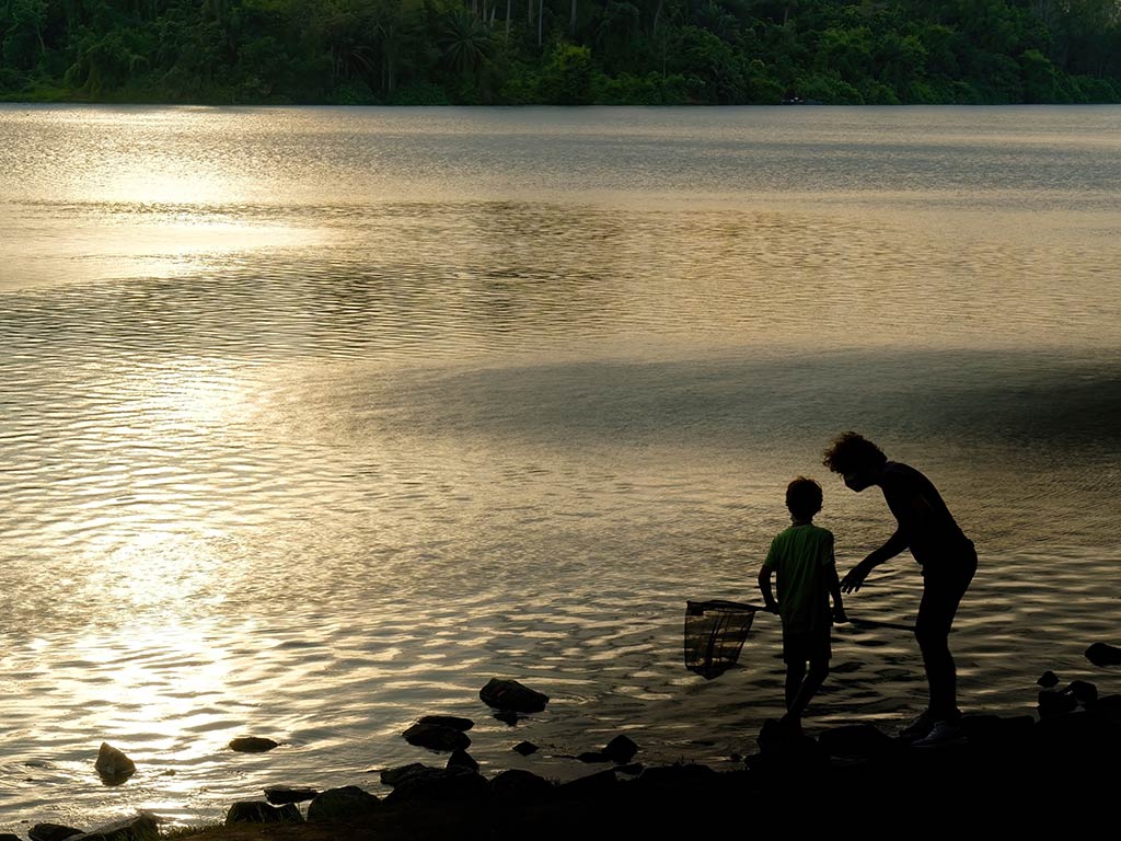 A silhouette of a parent helping a child with a fishing net on a lake in Singapore on a very sunny day