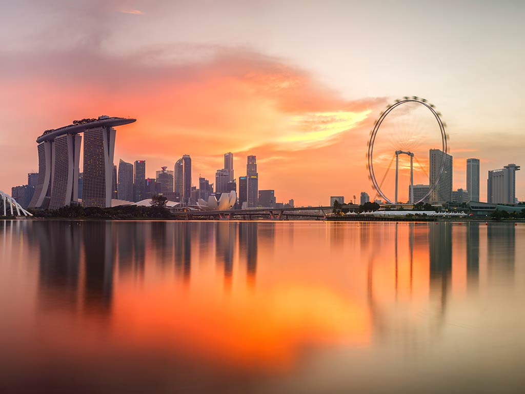 A view across the water from behind the Marina Sands Bay hotel at sunset with a ferris wheel visible in the distance