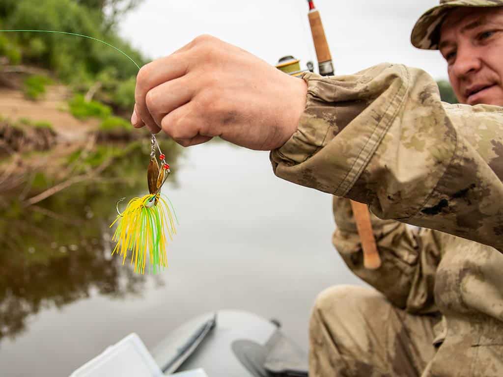 A closeup image of a spinnerbait stuff used as lure on the end of a fishing line stuff held by a male angler on a wend on a cloudy day