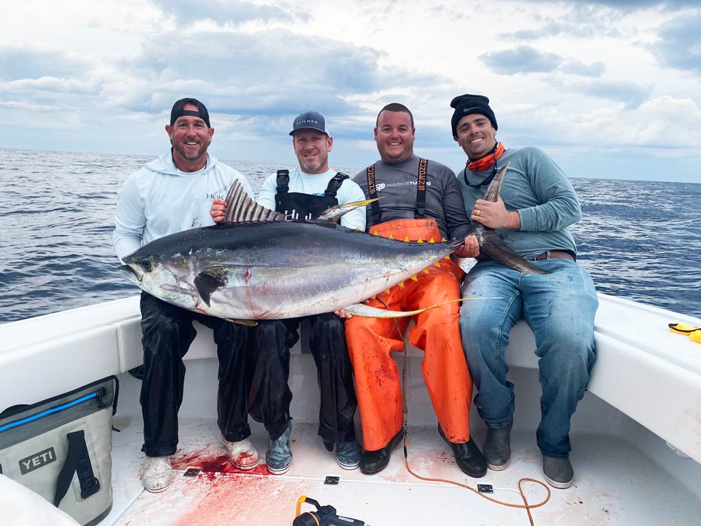 A group of fishermen standing on a Louisiana fishing boat, holding a big Yellowfin Tuna they caught on a cloudy day with blood on the deck of the boat