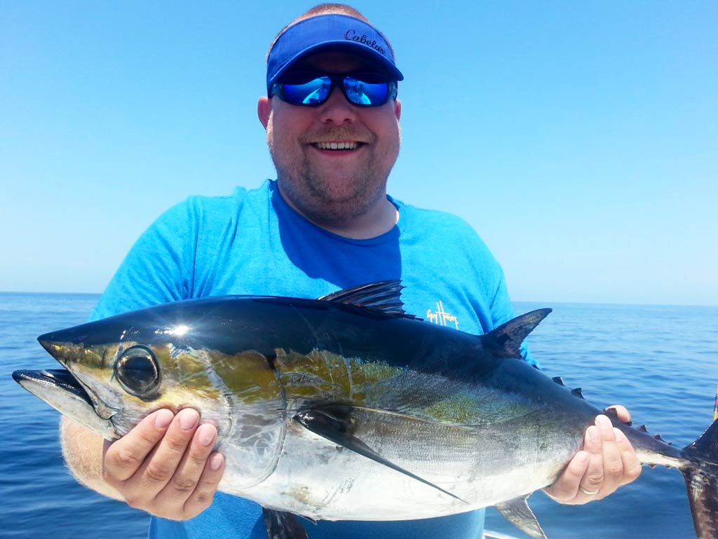 A photo of a satisfied angler smiling and holding Blackfin Tuna with both hands while standing on a Tybee Island deep sea fishing charter on a bright and sunny day