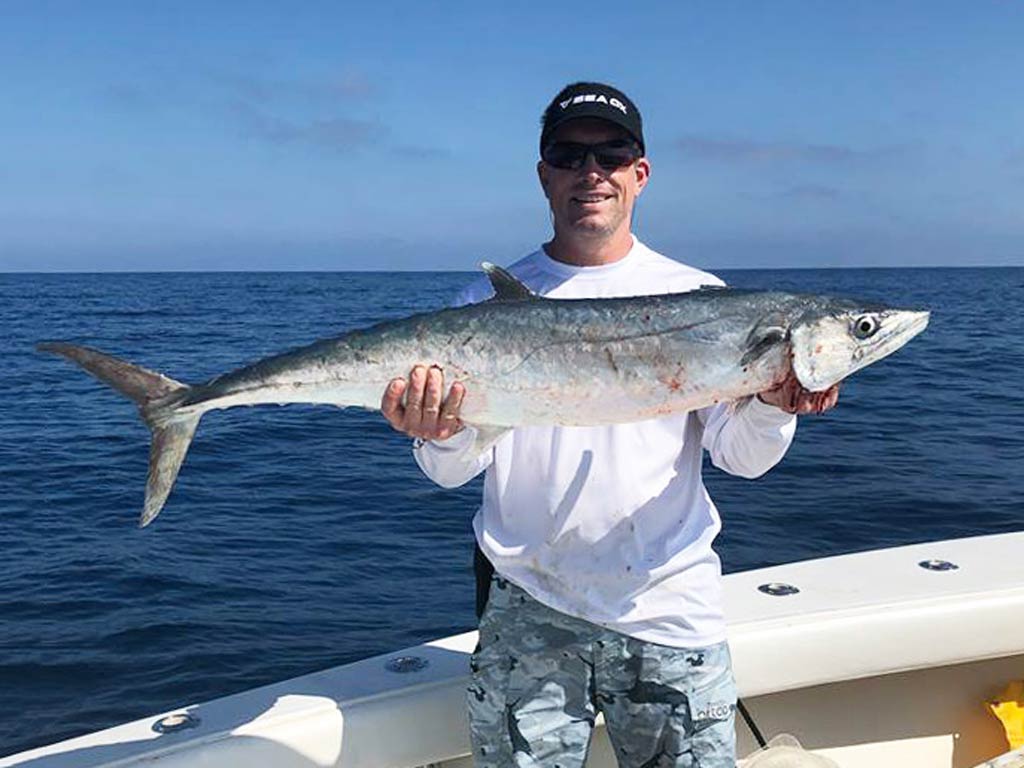 A photo of an angler standing on a charter boat and showing off a King Mackerel caught while fishing in Cudjoe Key in Florida on a sunny day