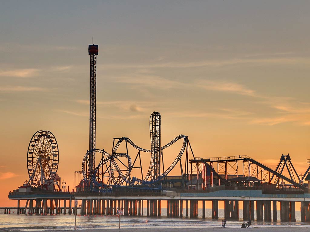 A view from the beach towards the amusement park at Galveston at sunset, with the ferris wheel on the far left