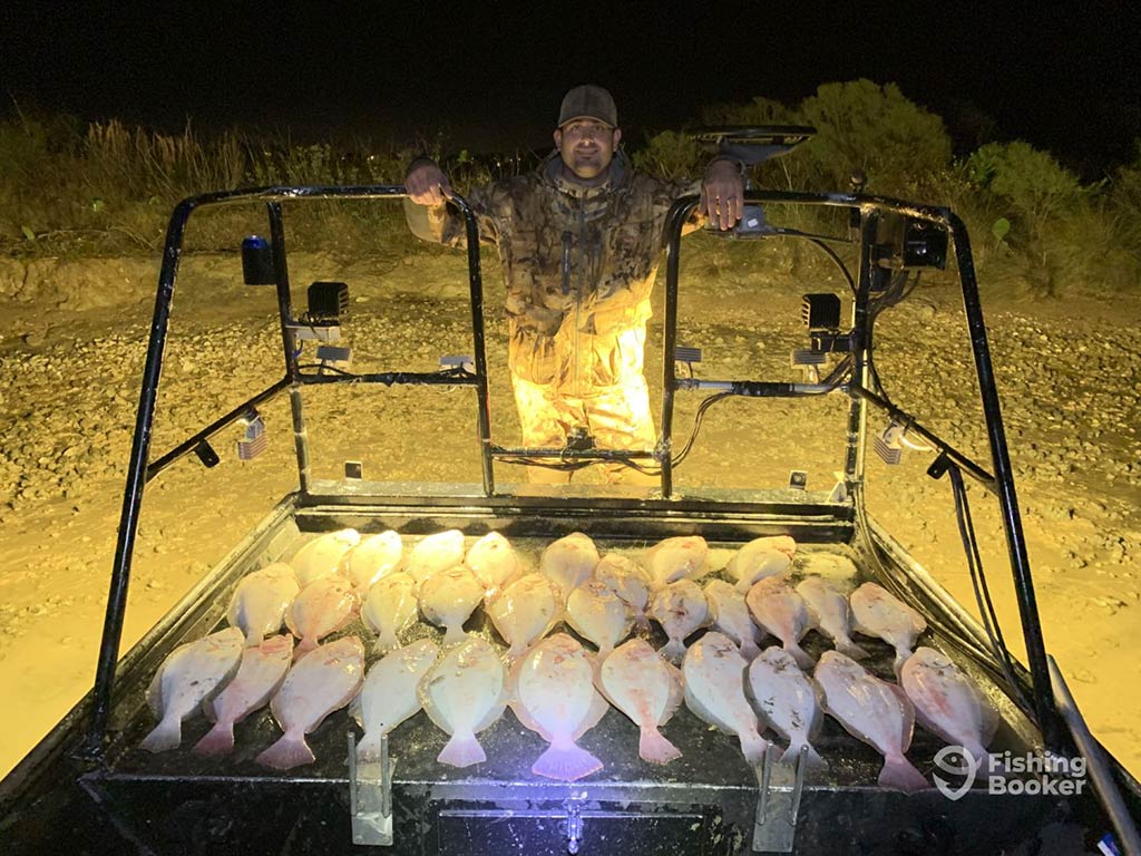 A man leaning over the back of his purpose-built flats fishing boat while back on dry land following a successful nighttime Flounder gigging trip in Galveston