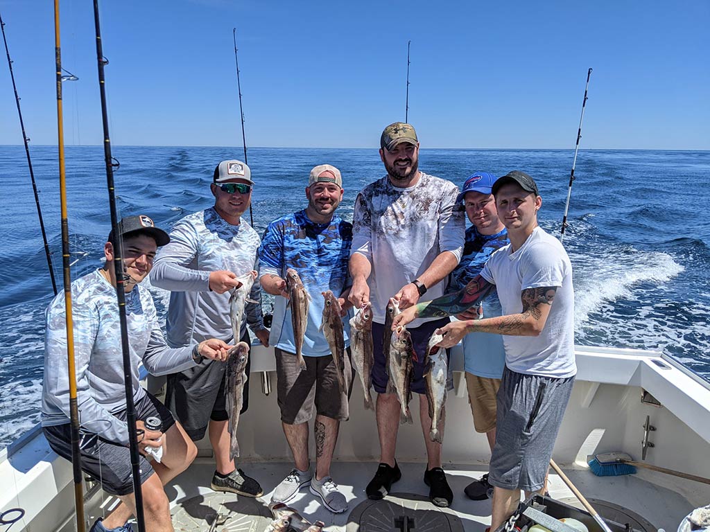 A group of anglers on a Gloucester fishing charter holding a load of Haddock with the water behind them and trolling rods set up all around them