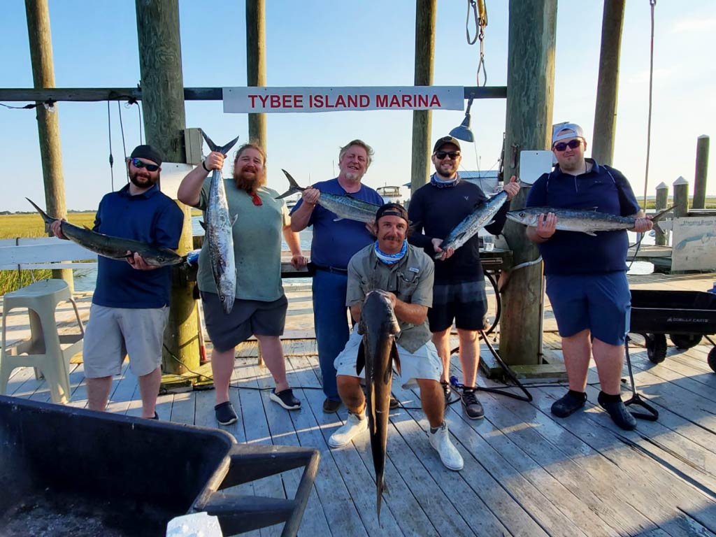 A group photo of six anglers posing with their fish caught on a deep sea fishing trip on the wooden dock of Tybee Island Marina