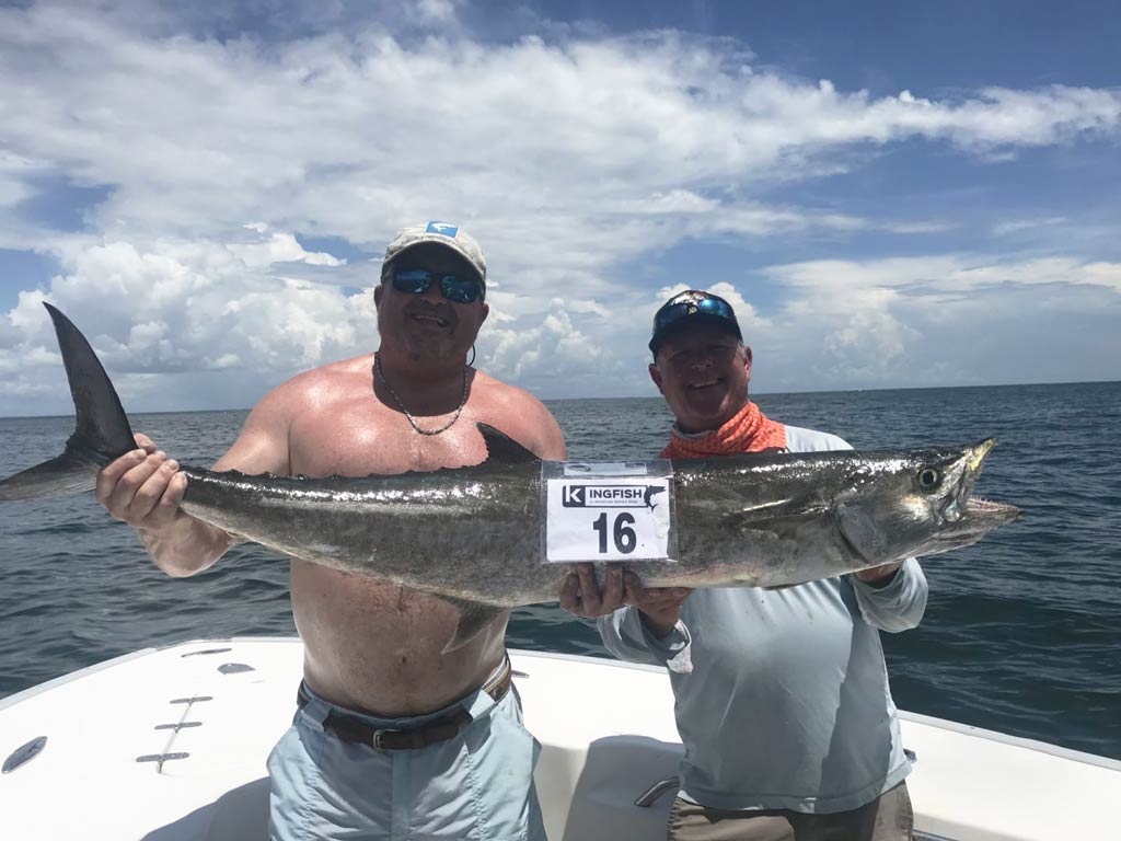 A photo of two proud anglers wearing caps while posing on a charter fishing boat with their big King Mackerel caught on a Tybee Island deep sea fishing trip