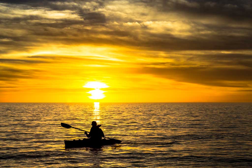 A man on a kayak, paddling in the open water during the sunset