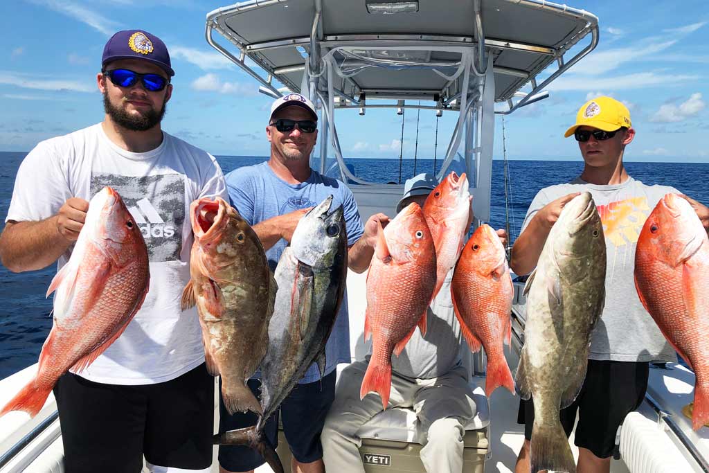 A group of three men on a center console fishing boat, each holding a mix of Snapper, Grouper and one Blackfin Tuna