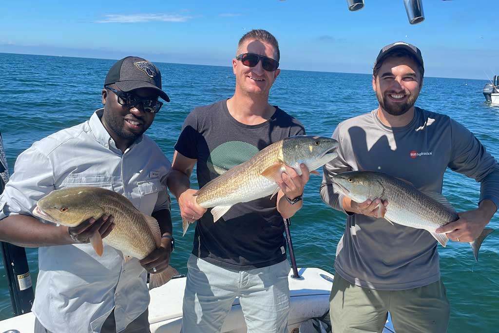 Three fishermen on a boat, each holding a Redfish they caught