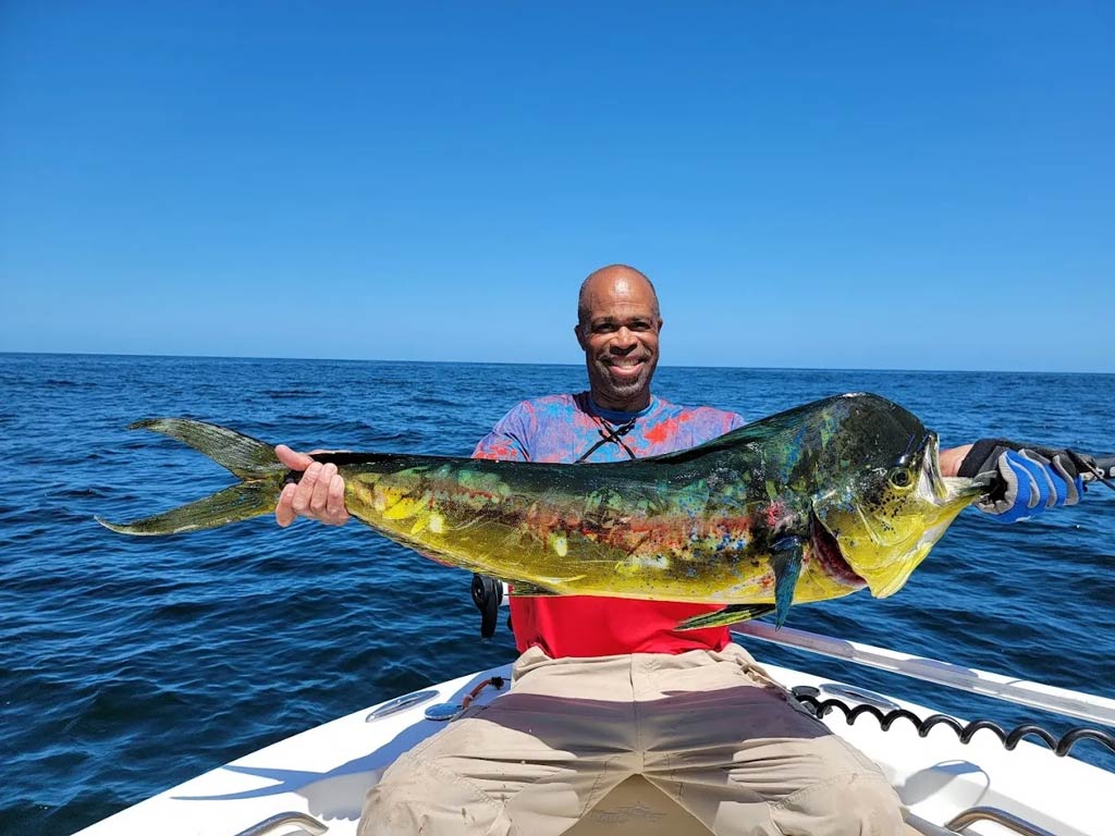 A photo of an angler sitting on a charter fishing boat and holding a big Mahi Mahi caught while deep sea fishing off St. Simons Island on a bright and sunny summer day