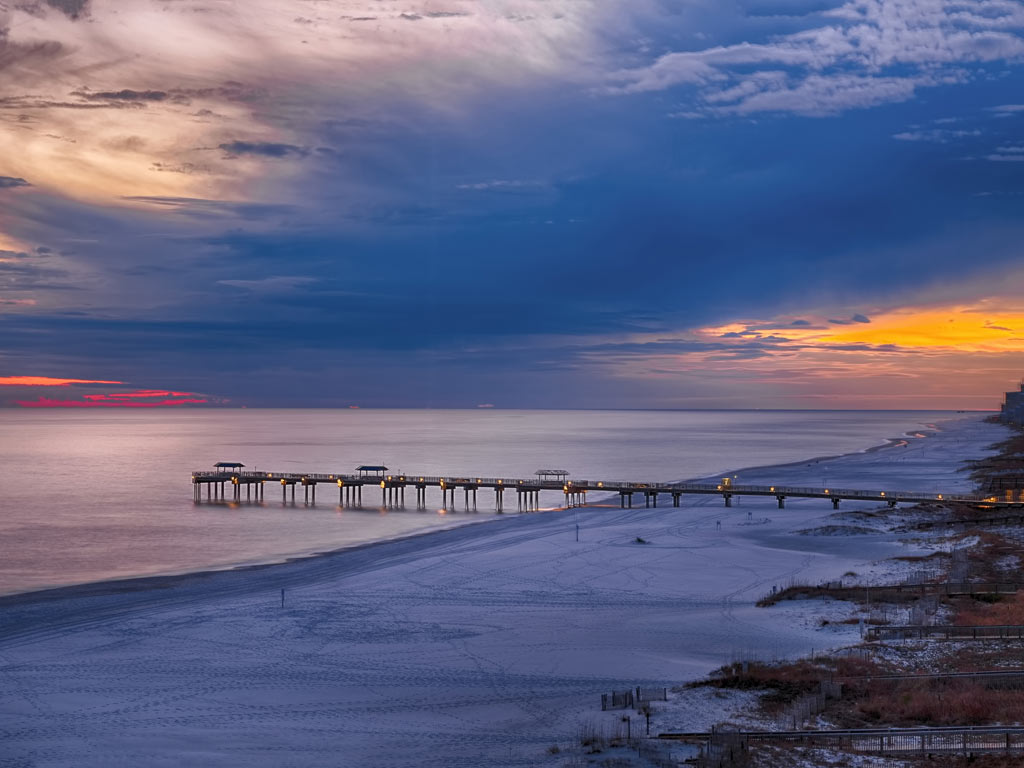 A photo of the Orange Beach fishing pier at sunset, with a thick layer of clouds in the skies.