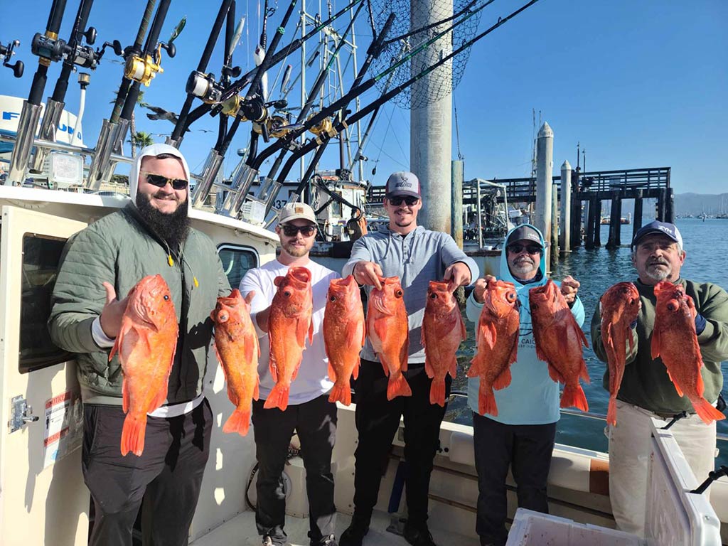 A group of male anglers of different ages, standing on a fishing charter back at the dock, holding two bright red-orange Rockfish each on a sunny day