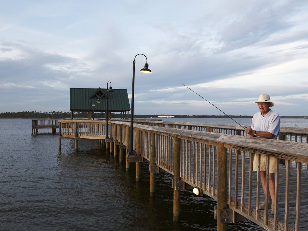 An elderly man fishing from a dock near Orange Beach, Alabama. He's in the forefront of the photo while the dock extends behind him.