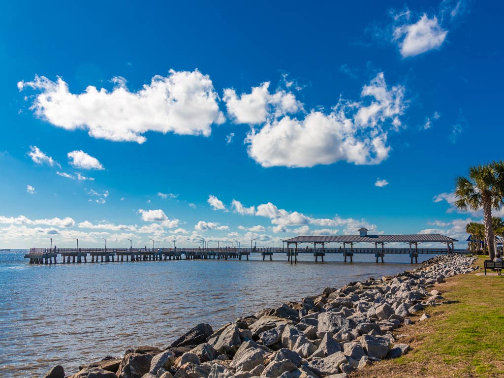 A photo featuring St. Simons Island Pier stretching into the Atlantic during a bright and sunny day, with the sky full of white clouds